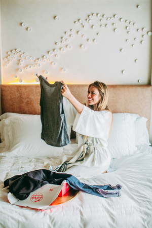 A blonde woman in a white bedroom holds up a grey tank top from her YogaClub box