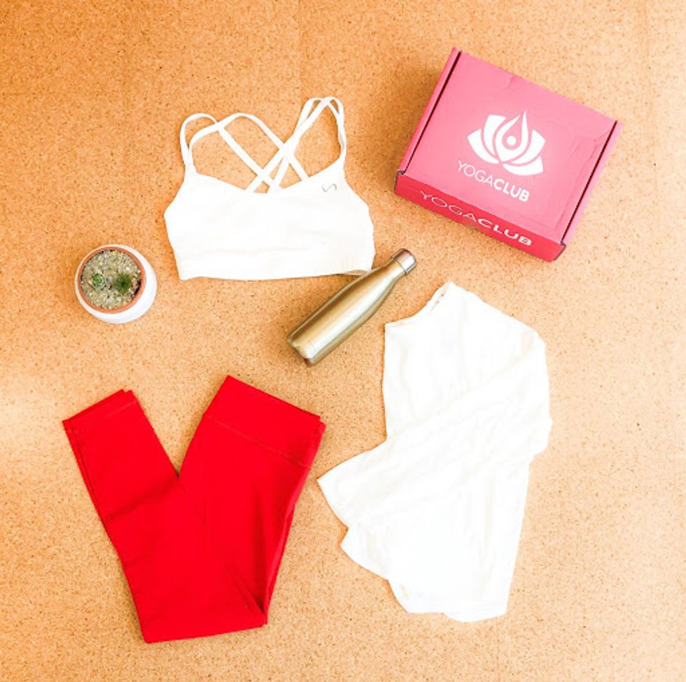 a matching set of white yoga clothes with red pants, a water bottle, and a yogaclub box