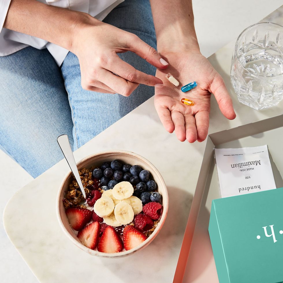 Hands holds supplements and vitamins with a breakfast bowl and a personalized vitamin pack