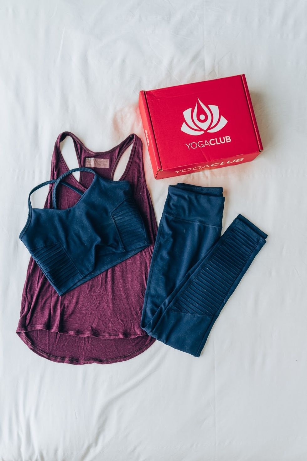 A matching set of blue yoga clothes with a pink tank top next to a yogaclub box