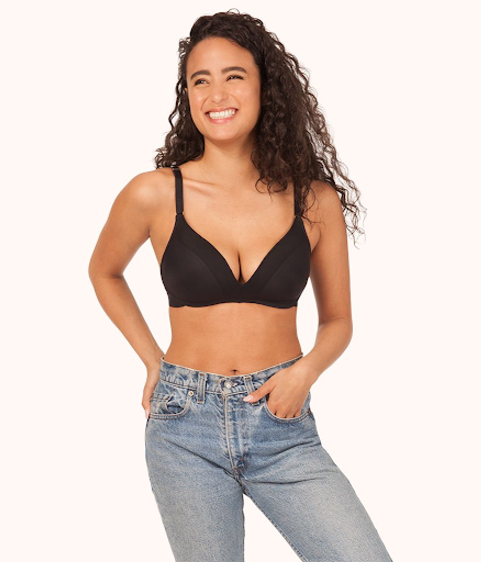 A curly-haired brunette in a black Lively bra and jeans smiles